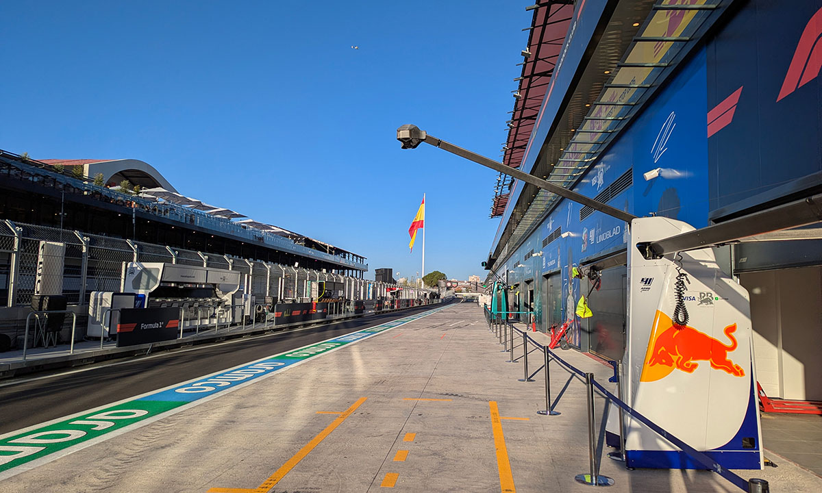 Madring-F1-circuit-LDA-references-09 Empty MADRING pit lane lined with team garages and a Spanish flag under a clear blue sky